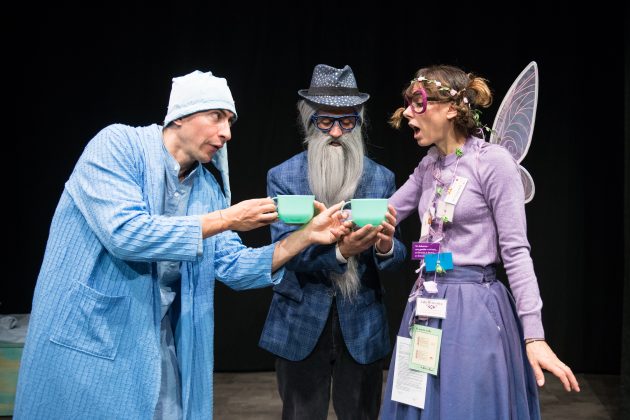 re attori interpretano una Fata con ali e occhiali rosa, un Mago con barba lunga grigia e un Principe in pigiama azzurro. I tre brindano con grandi tazze color menta, con espressioni stupite e divertite, sul palco dello spettacolo Sfavola.
